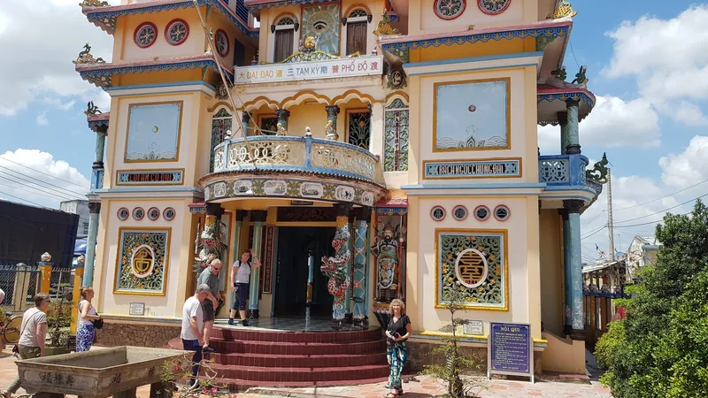 Visitors gather outside the ornate, colorfully decorated Cao Dai temple facade in the Mekong Delta.