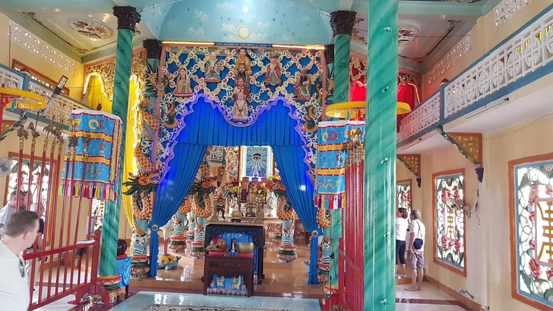 Colorful interior of a Cao Dai temple in the Mekong Delta with ornate blue curtains and the Divine Eye altar.